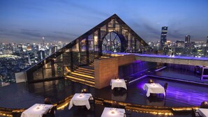 Un restaurant situé sur le toit d’un immeuble, avec des tables dressées pour le dîner, une structure en verre et une vue panoramique sur la ville.