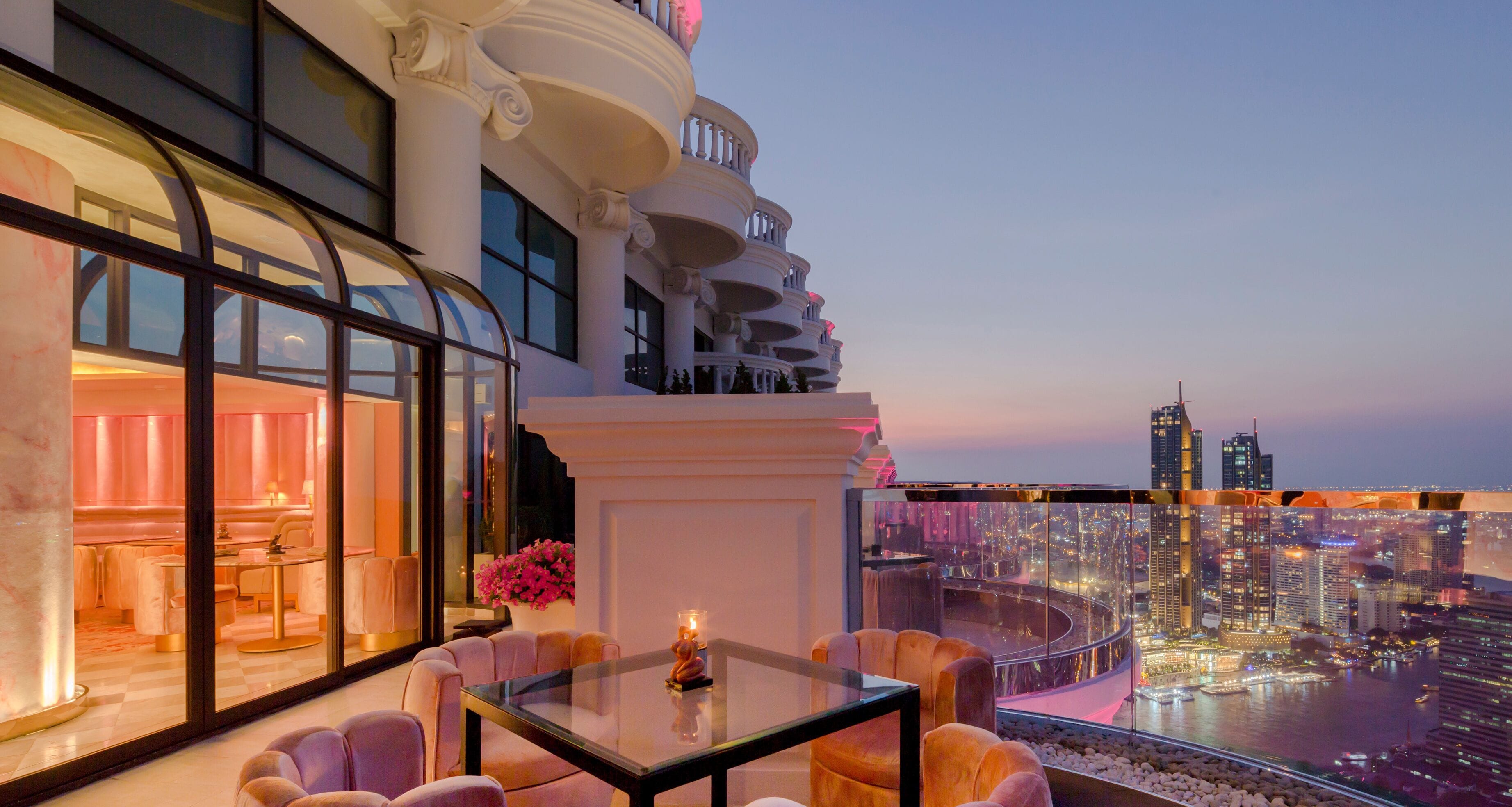 A luxurious balcony with a city view, elegant furniture, and a glass table.