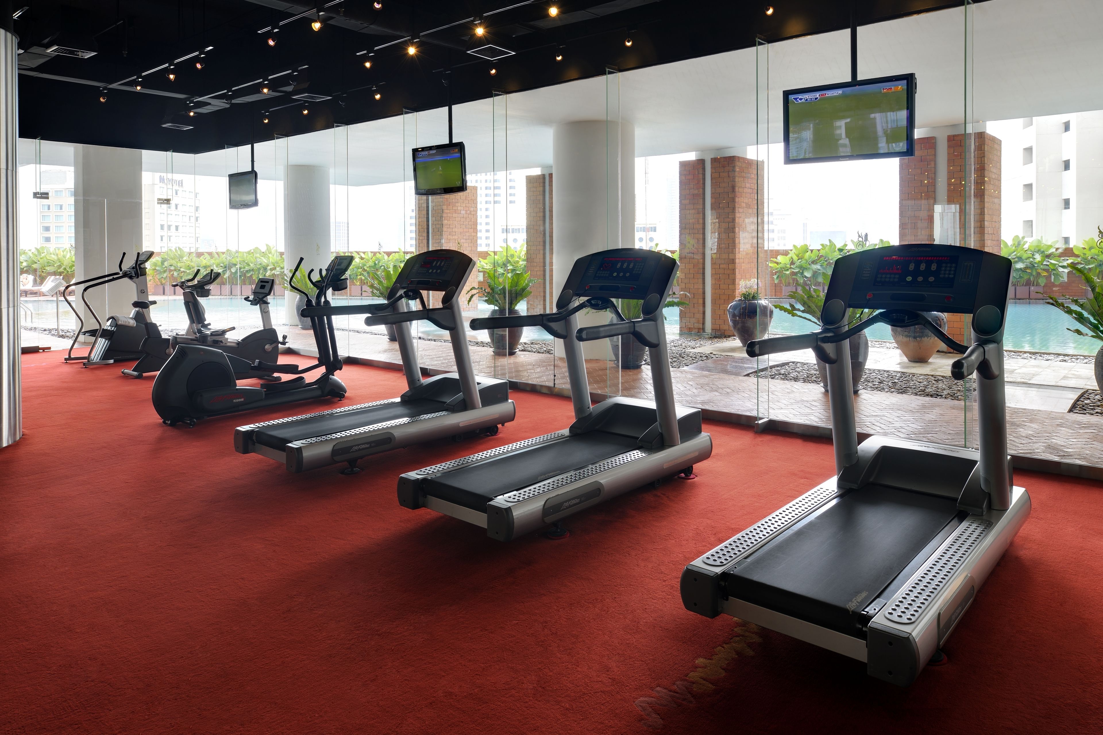 A gym with treadmills, stationary bikes, and a TV screen displaying a sports game.