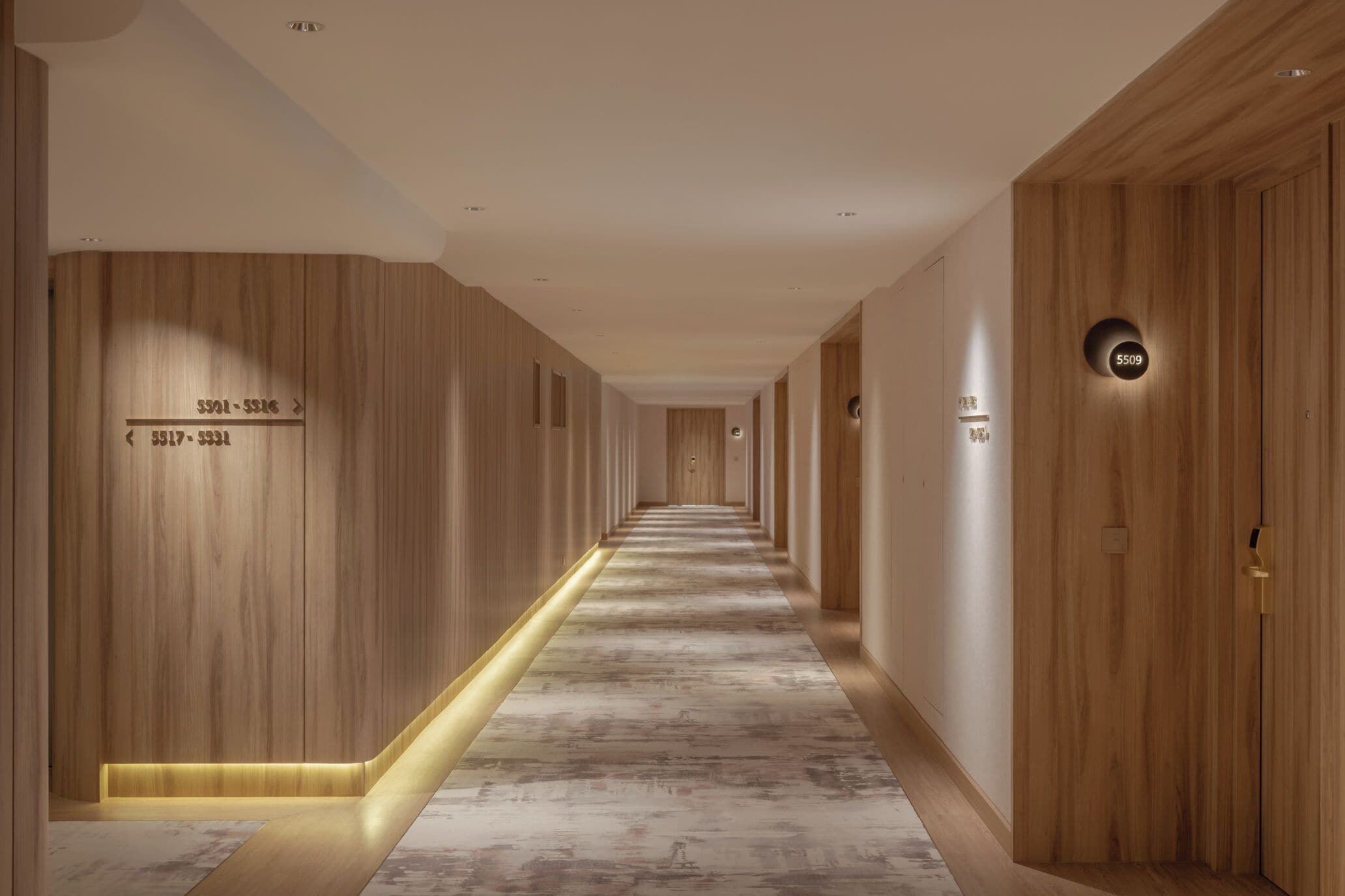 A modern hotel corridor with wooden paneling, numbered doors, and a marble floor.