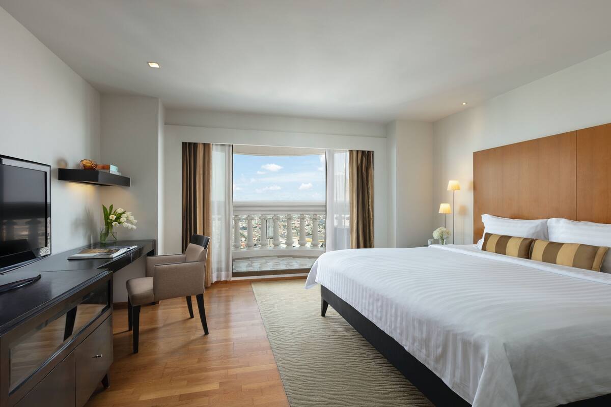 Ett hotellrum med en säng, ett skrivbord, en TV och en balkong med utsikt.
