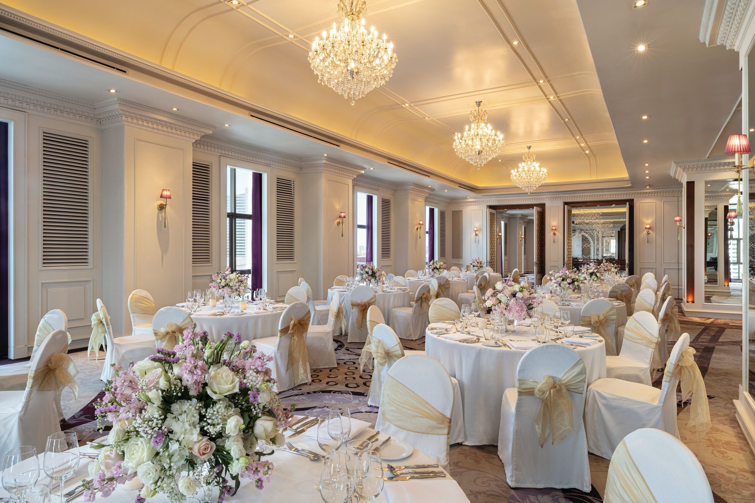 Un salón de banquetes con mesas redondas, sillas blancas y candelabros.