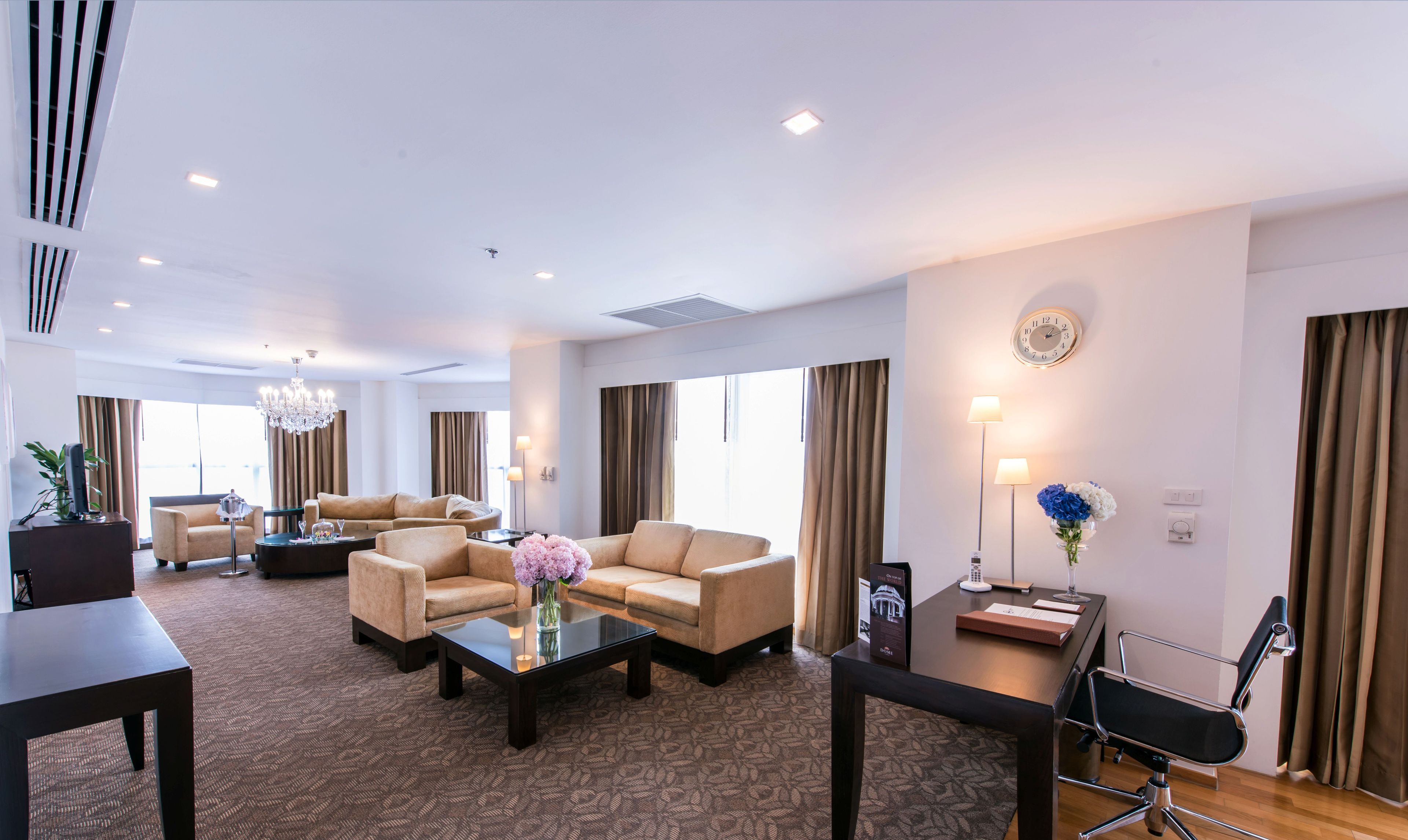 A spacious hotel living room with a sofa set, a coffee table, and a desk with a chair.