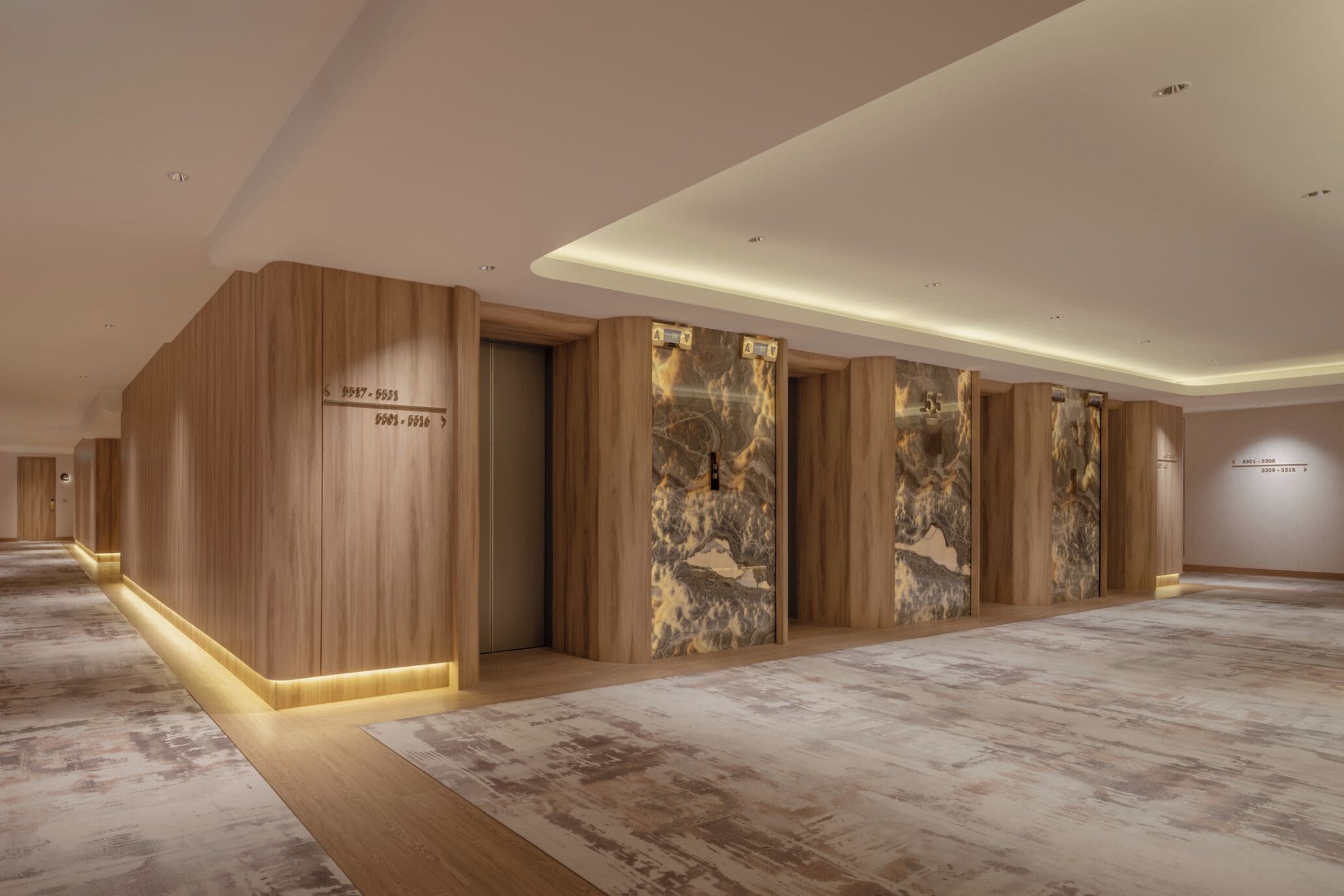 A modern hotel lobby with wooden paneling, marble flooring, and illuminated ceiling panels.