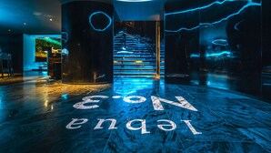 Un hall d’entrée moderne avec un sol en marbre, un escalier et un panneau lumineux au néon.