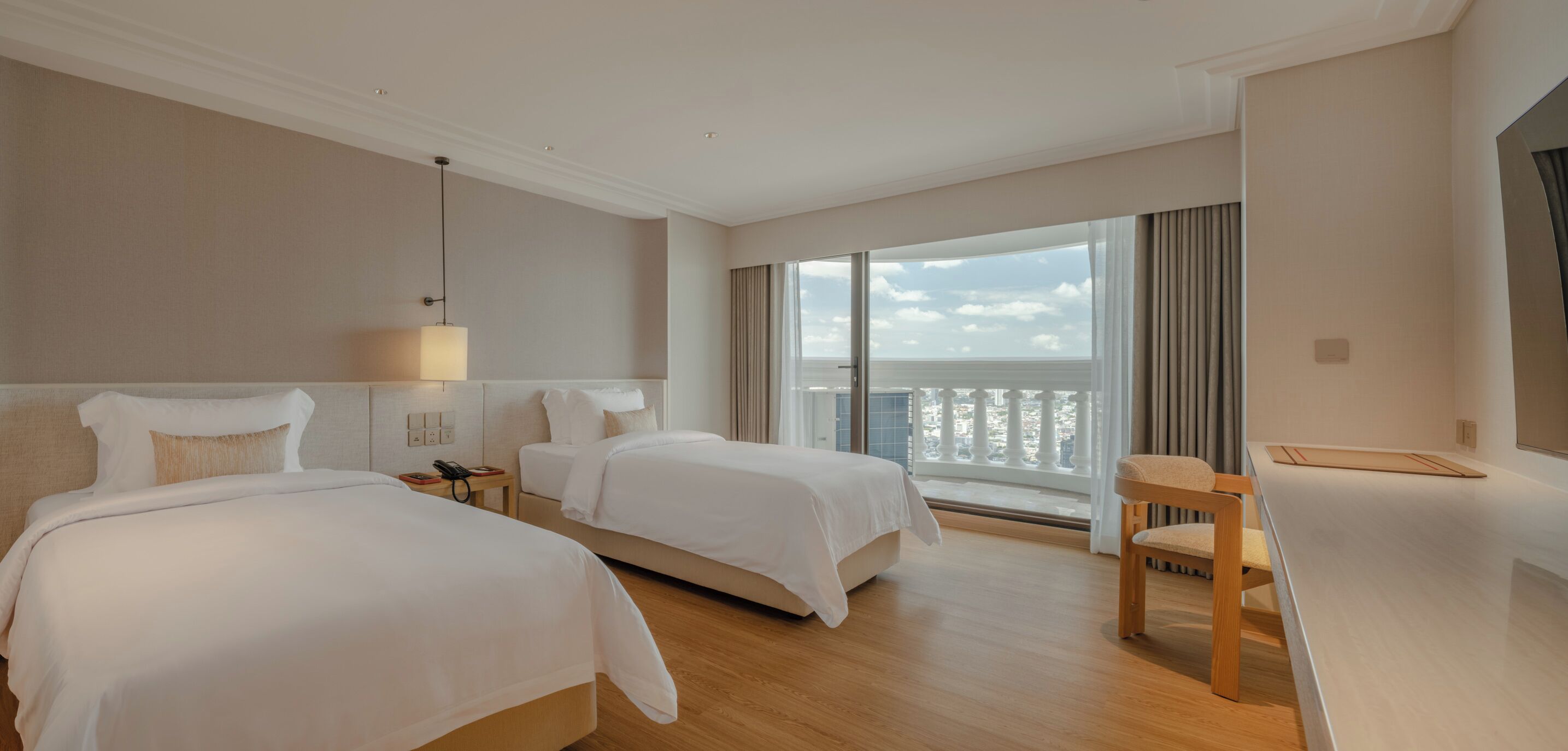 A hotel room with two beds, a desk, a chair, a lamp, and a large window with a view.