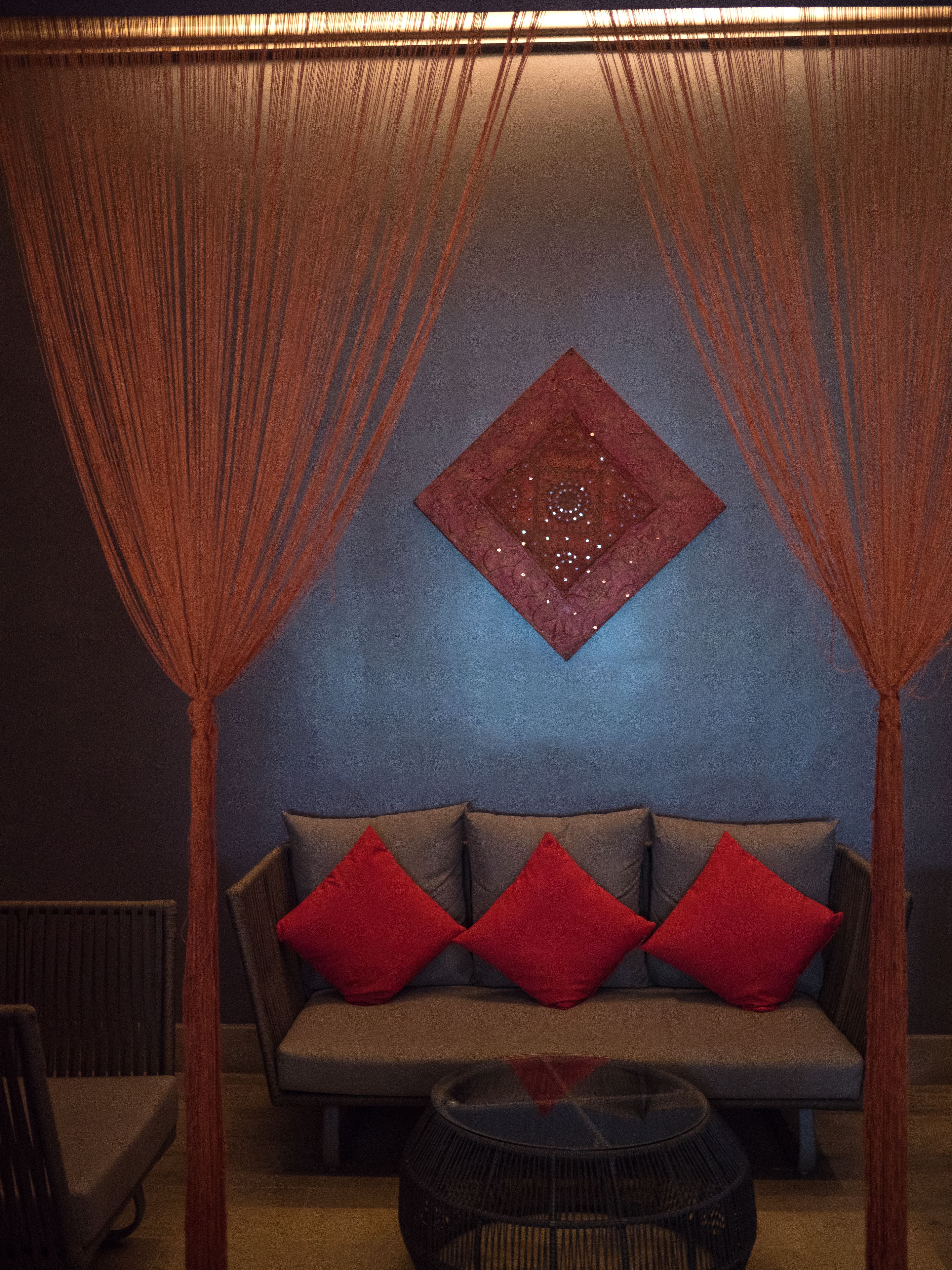 A room with a sofa, red cushions, a decorative wall piece, and a woven coffee table.