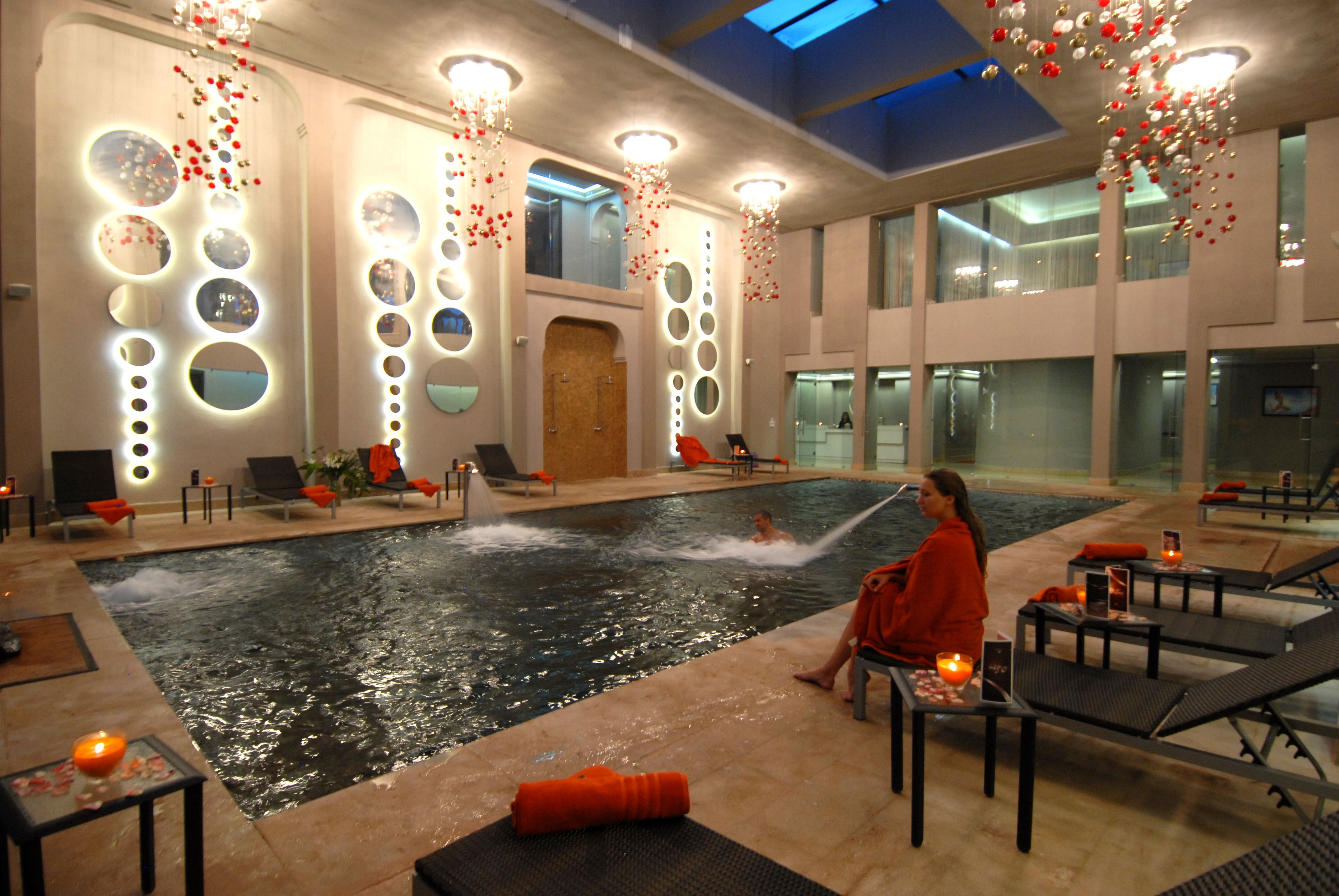 An indoor swimming pool with a person in the water, lounge chairs, and tables with candles.