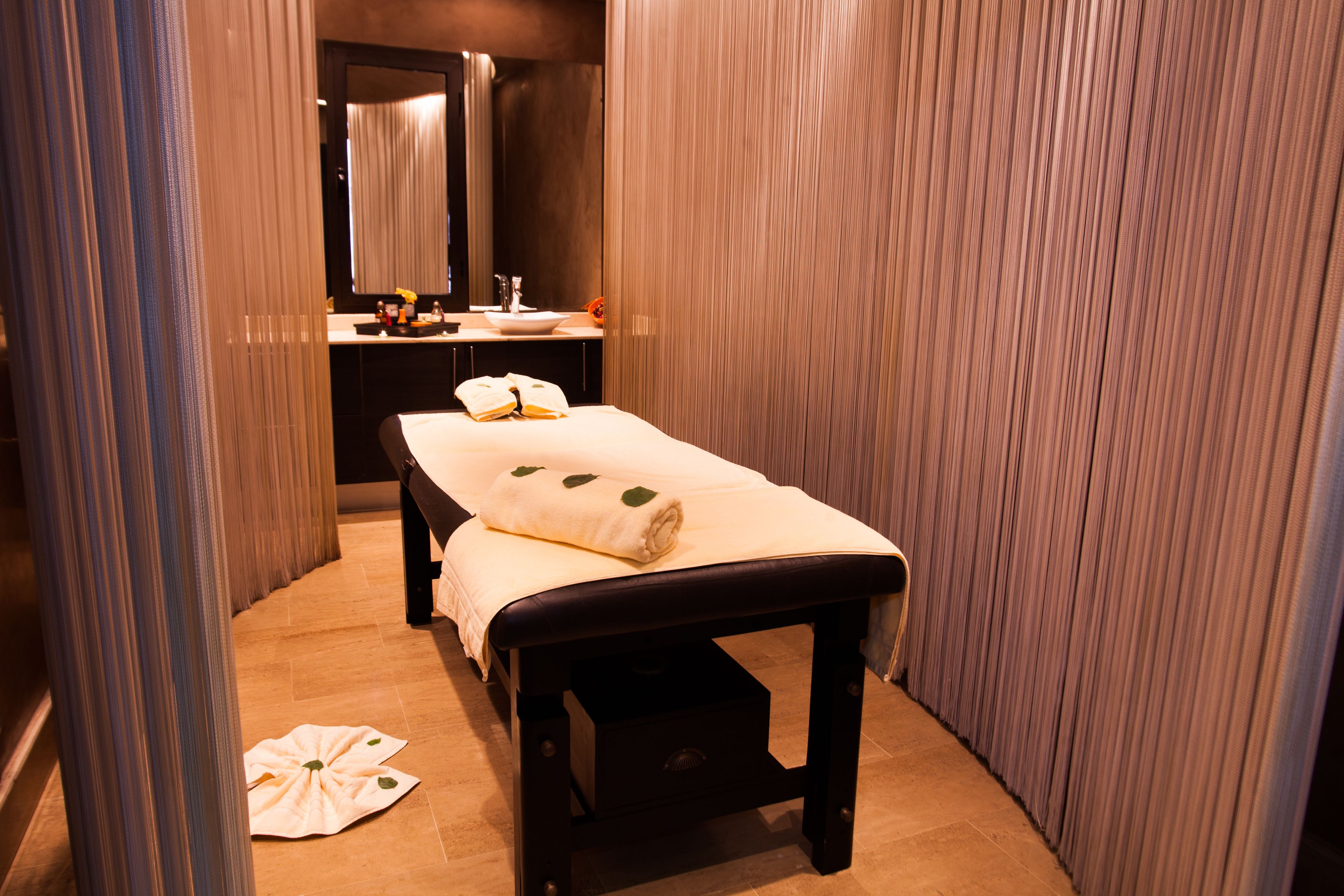 A spa room with a massage table, a sink, and a mirror.