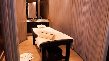A spa room with a massage table, a sink, and a mirror.