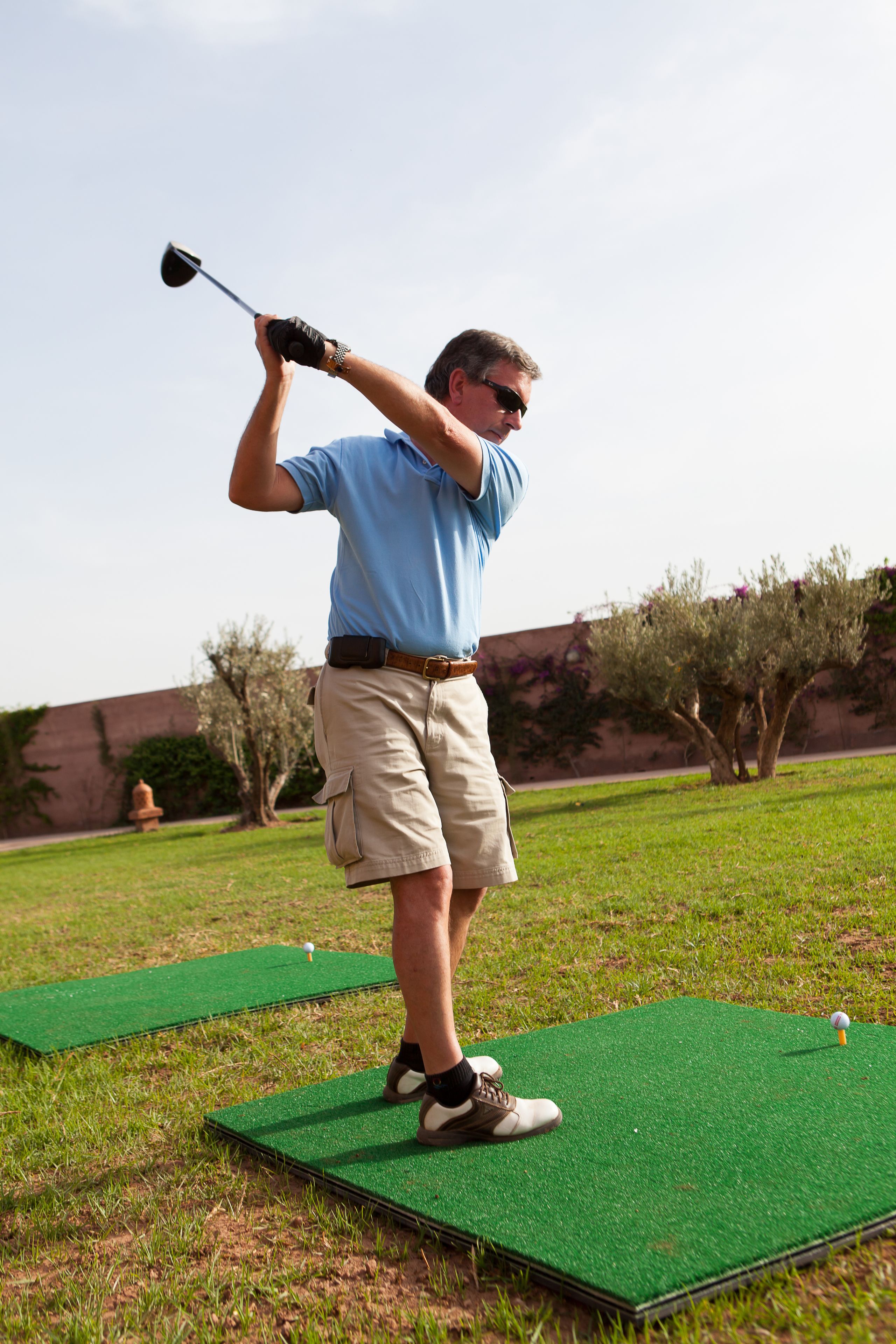 Una persona sobre una esterilla verde a punto de balancear un palo de golf.