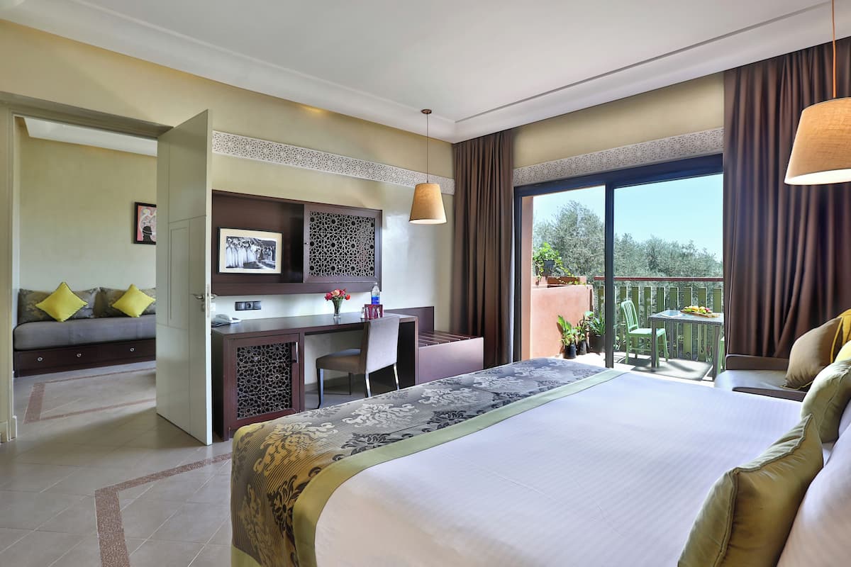 Habitación de hotel con una cama grande, un escritorio con silla, un balcón pequeño y vistas a zonas verdes.