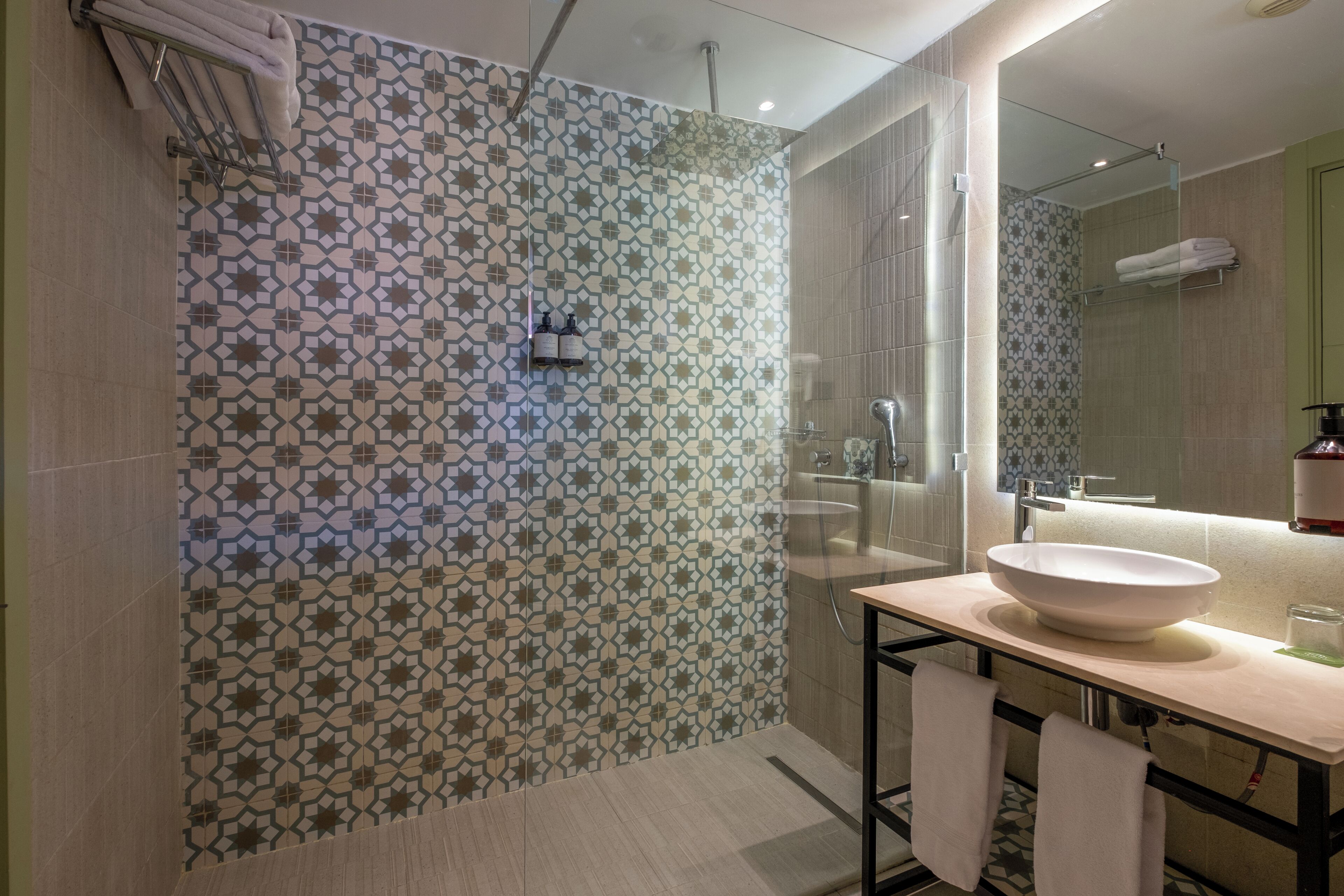 Un baño moderno con baldosas estampadas, un lavabo espacioso y una cabina de ducha con paredes de cristal.