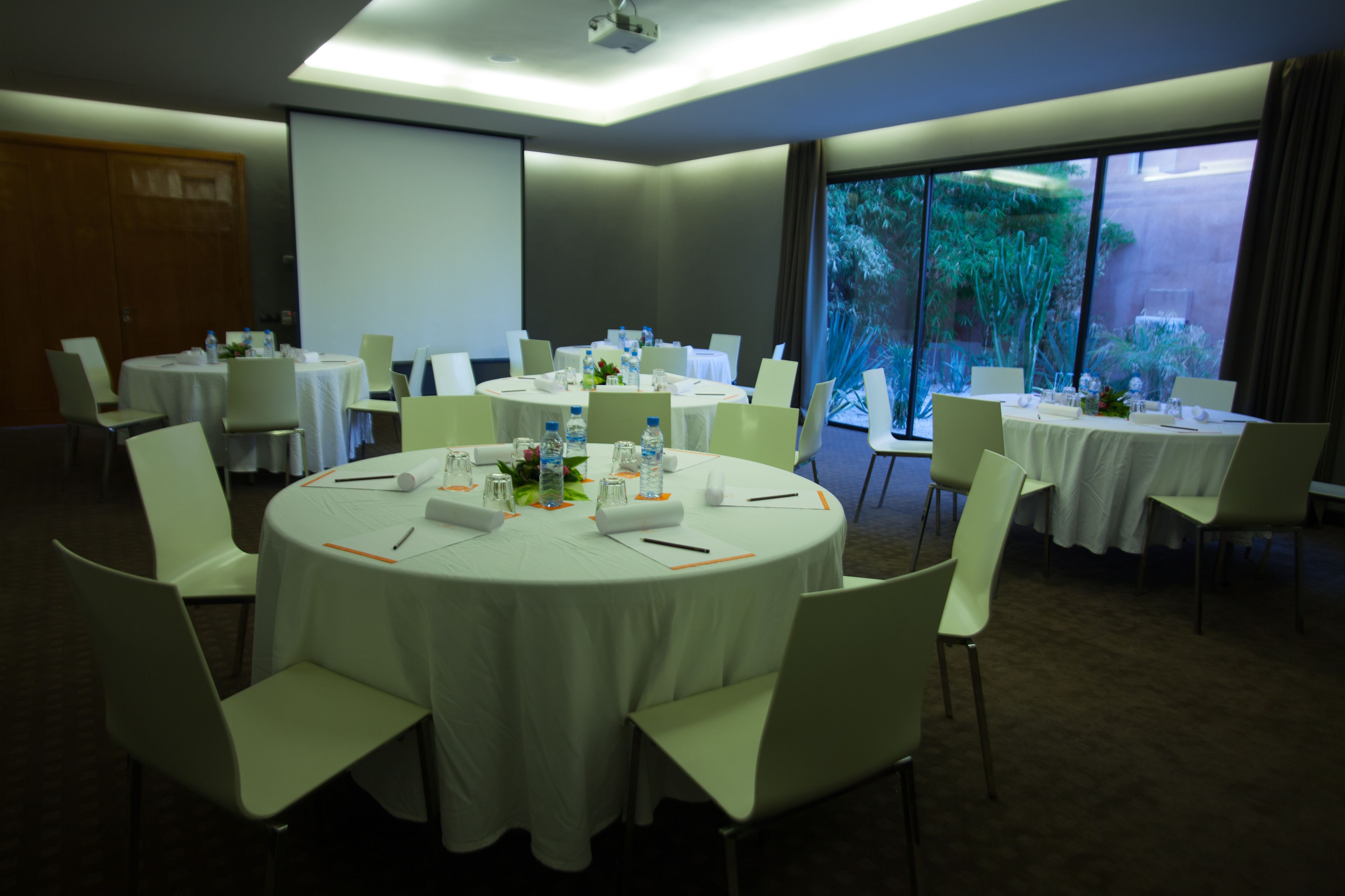 A conference room with multiple round tables, white chairs, and a projector screen.
