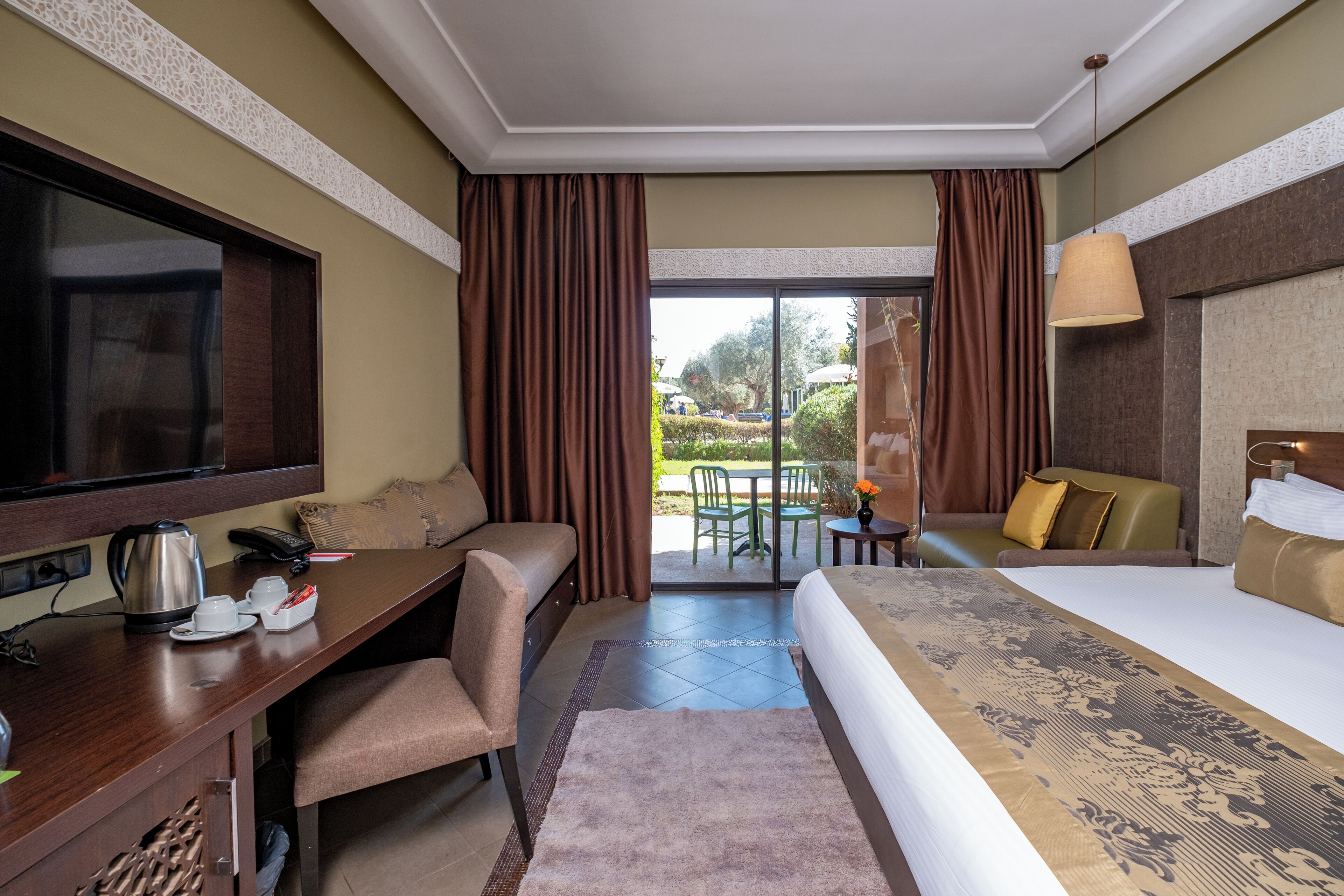 A hotel room with a bed, a desk, a television, a coffee maker, and a view of the outdoors.