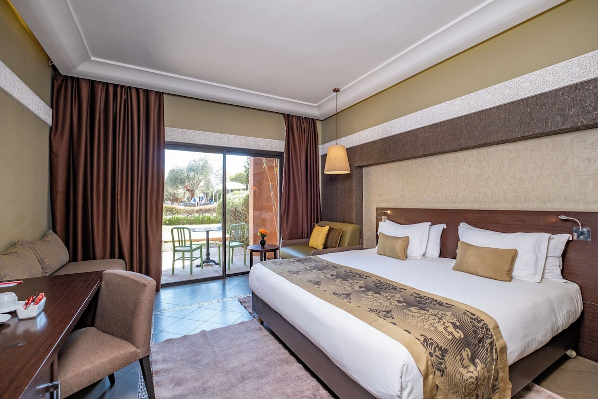 Habitación de hotel con una cama grande, un escritorio con silla, una mesita con silla y vistas al exterior.