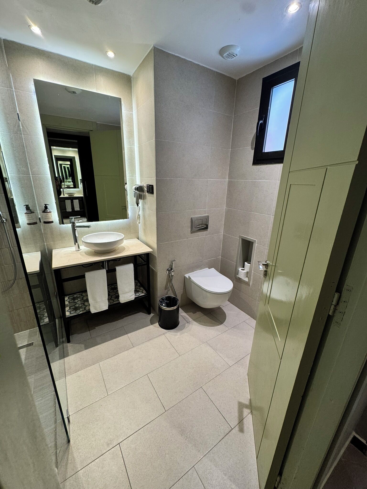 Un baño moderno con un espejo grande, un lavamanos, un inodoro y una zona de ducha.