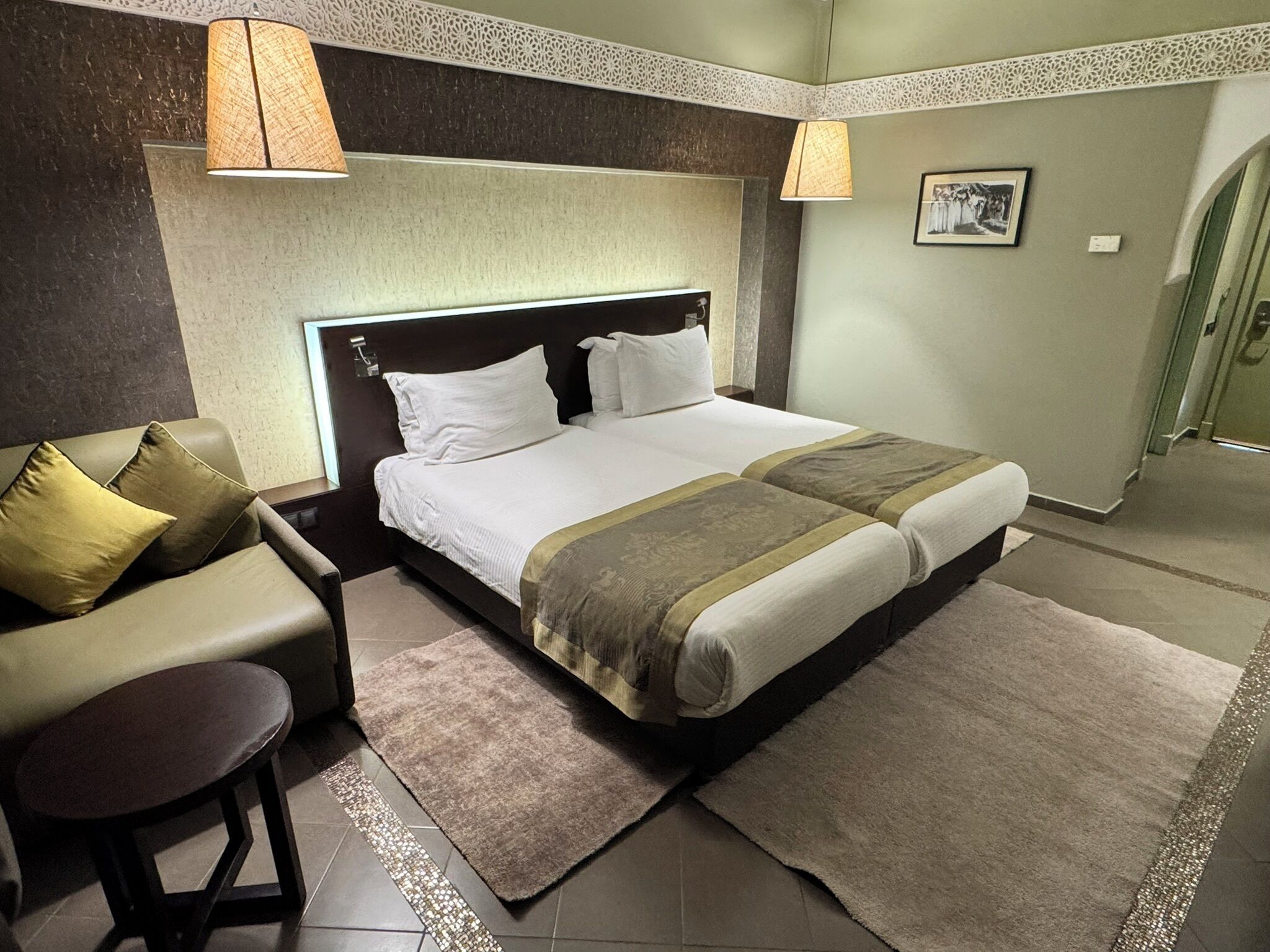 A hotel room with a bed, a sofa, a small table, and a door leading to a bathroom.