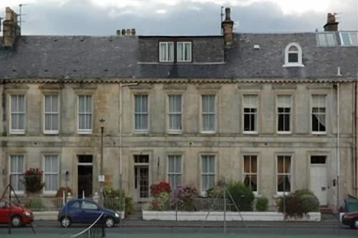 A two-story building with a stone facade, multiple windows, and a red sports court in front.