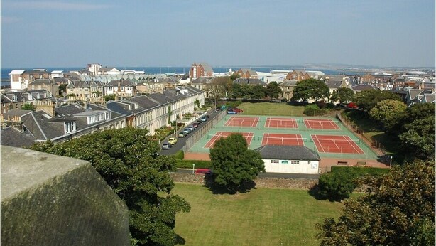 Ein Tennisplatz, umgeben von Wohnhäusern und einem großartigen Steinbau.