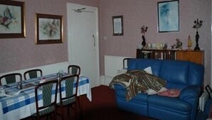 Ein Zimmer mit Esstisch für vier Personen, einem blauen Sofa und einer Tür mit weißem Rahmen.
