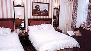 Ein Hotelzimmer mit zwei Betten, einem großen Spiegel, einem Gemälde an der Wand und einer Tür mit Vorhängen.