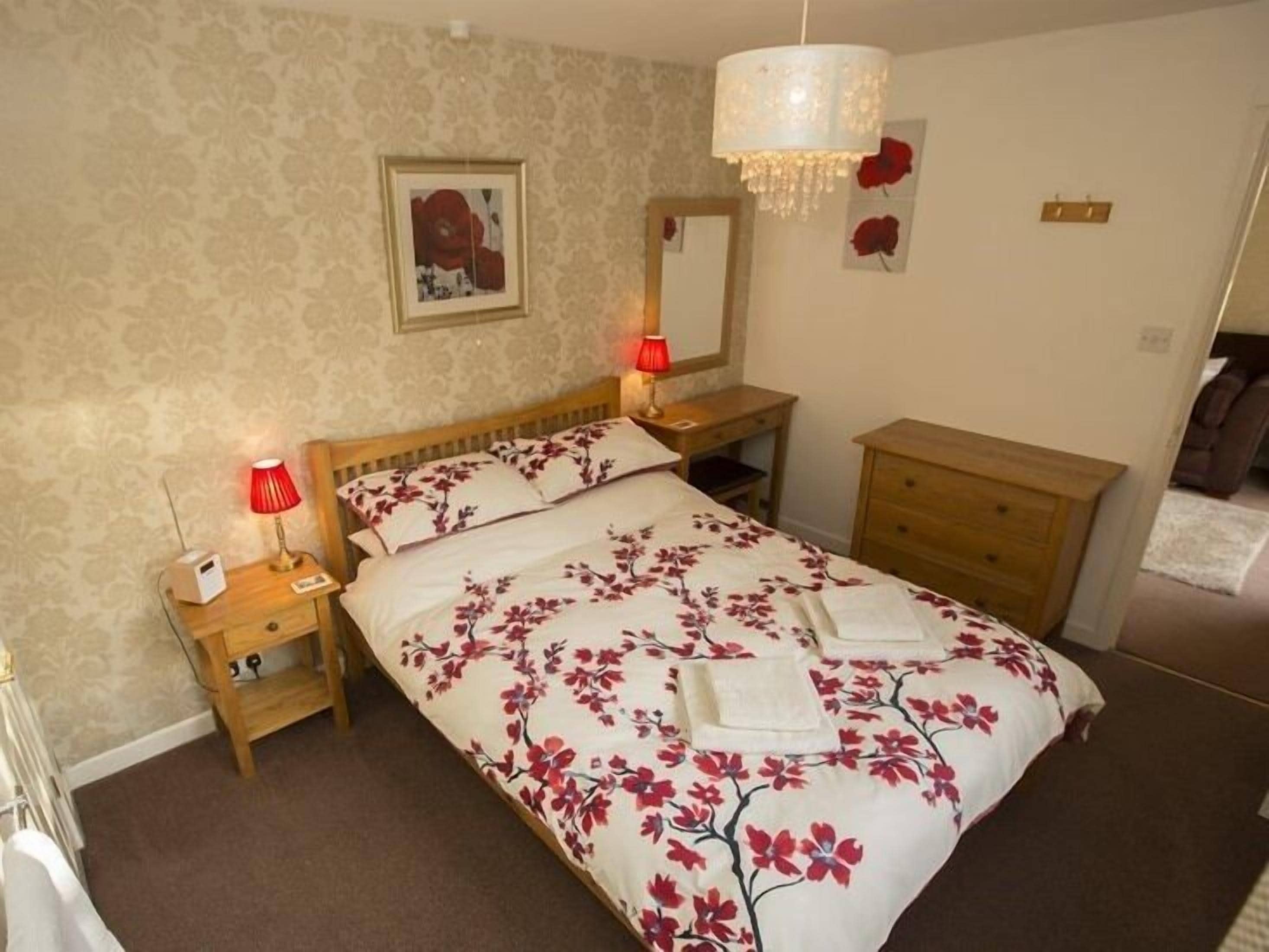 A bedroom with a bed, bedside tables, a dresser, a mirror, and a chandelier.