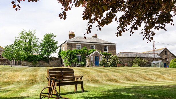 A rustic stone building with a blue door, surrounded by a well-maintained lawn and trees. - Smeaton Farm (Saltash)