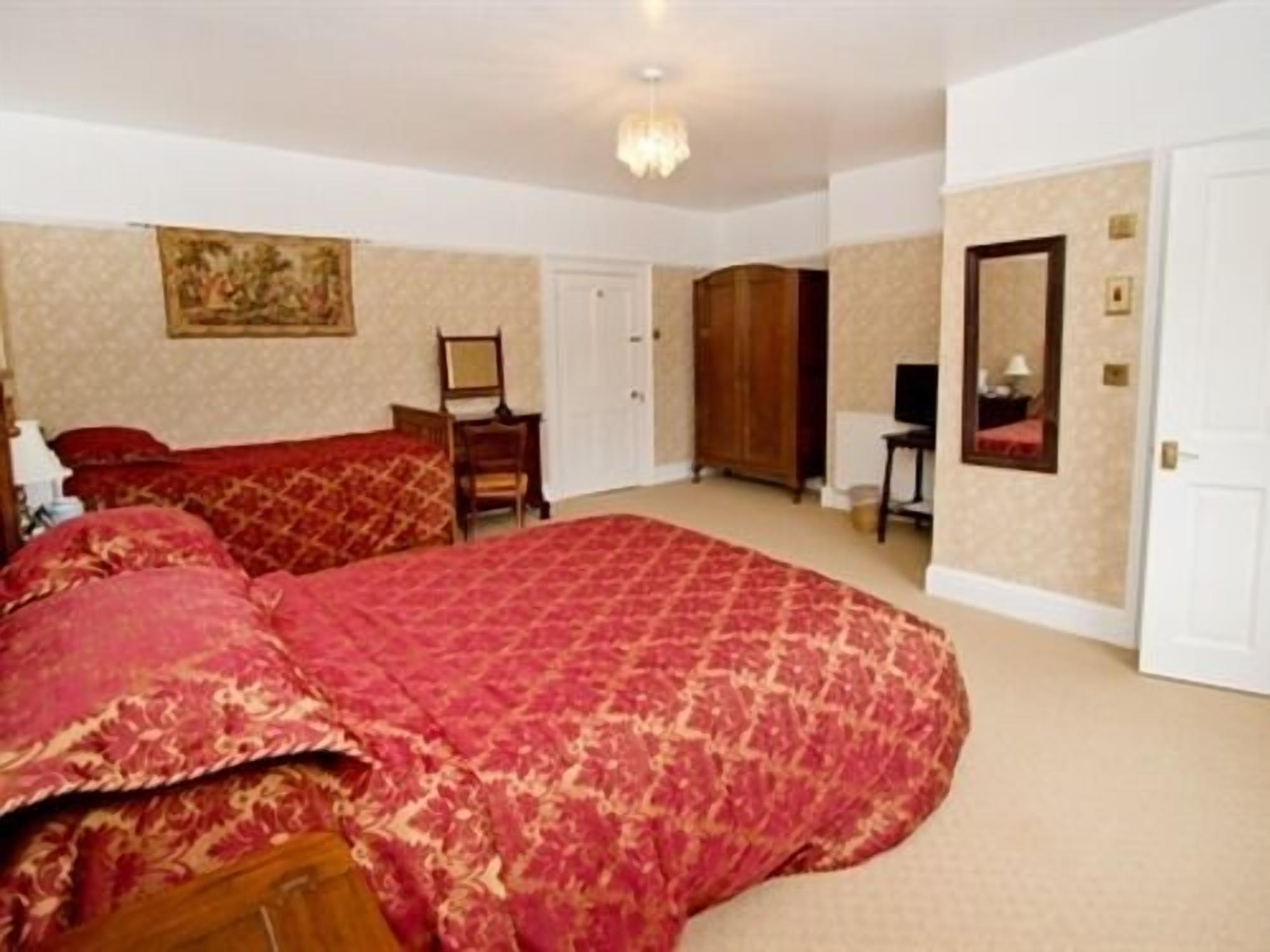A bedroom with a large bed, a wardrobe, a desk, and a mirror.