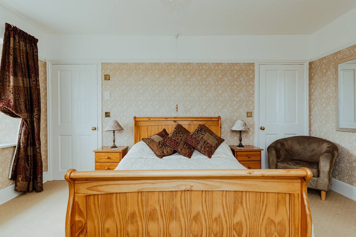Een slaapkamer met een houten bed, kamerbreed gordijn en een stoel.