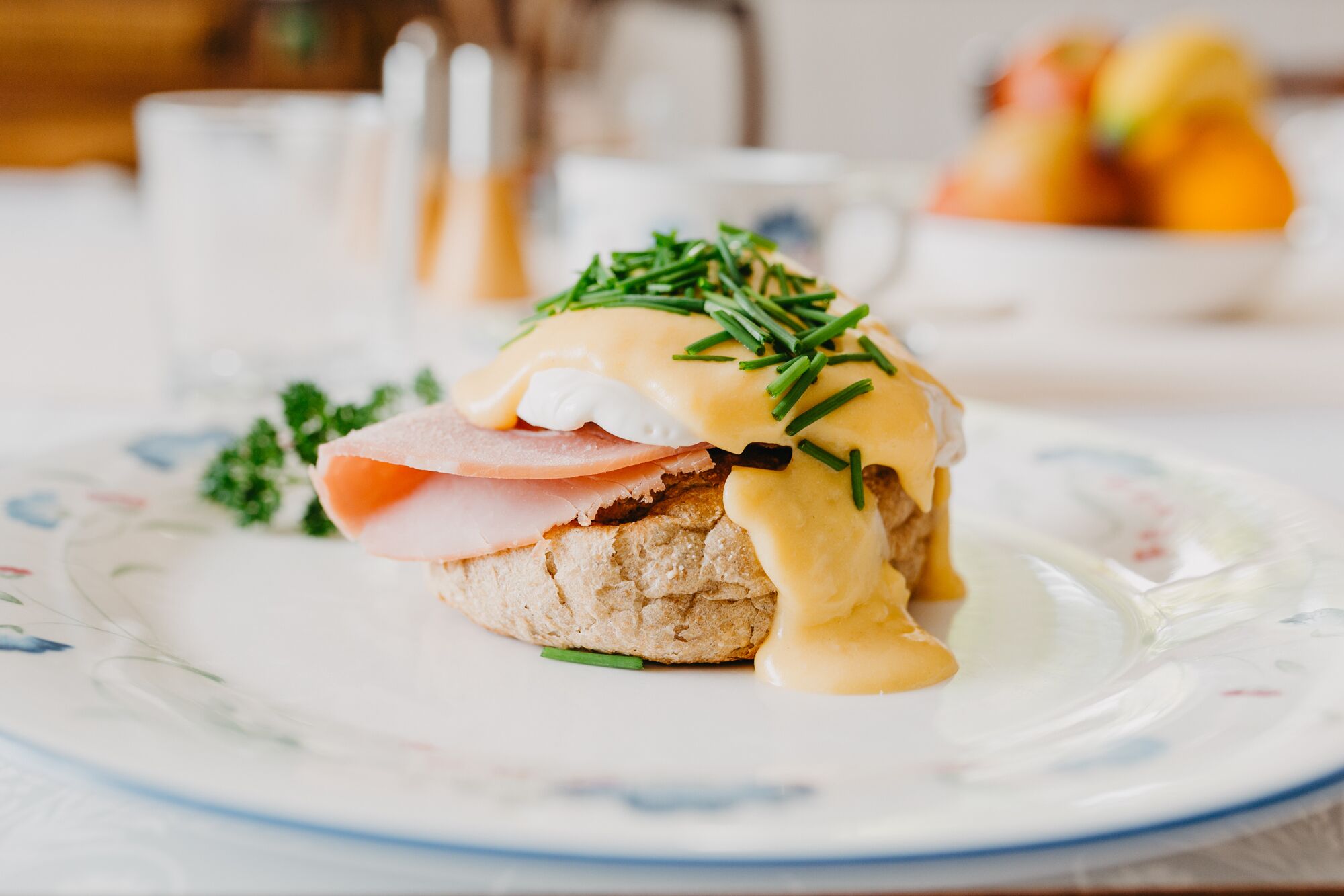 A breakfast plate with eggs benedict, ham, and chives on a floral-patterned plate.