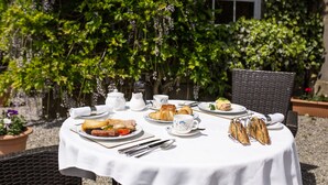 An outdoor dining table set with various breakfast items, surrounded by wicker chairs and a backdrop of lush greenery. - Smeaton Farm (Saltash)