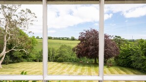 A view through a window of a well-maintained lawn with a variety of trees and a distant hill. - Smeaton Farm (Saltash)