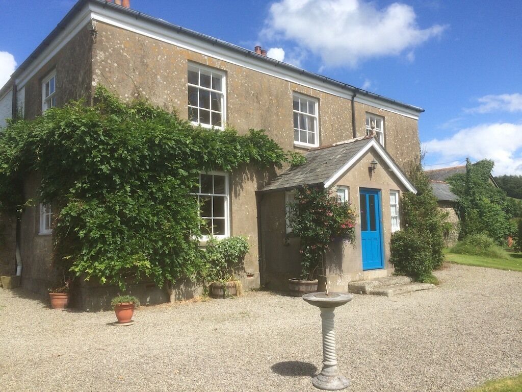 A two-story house with a blue door, surrounded by potted plants and a gravel driveway.