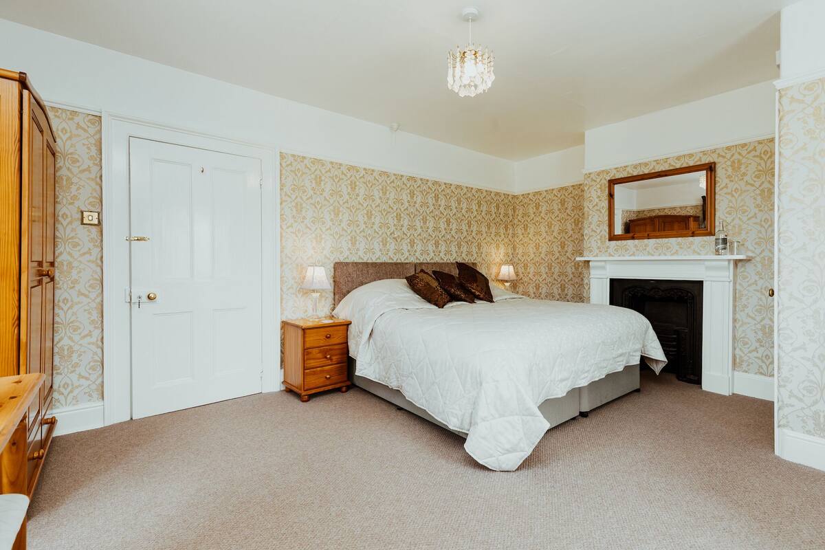 Een slaapkamer met een bed, nachtkastje, dressoir en een open haard.