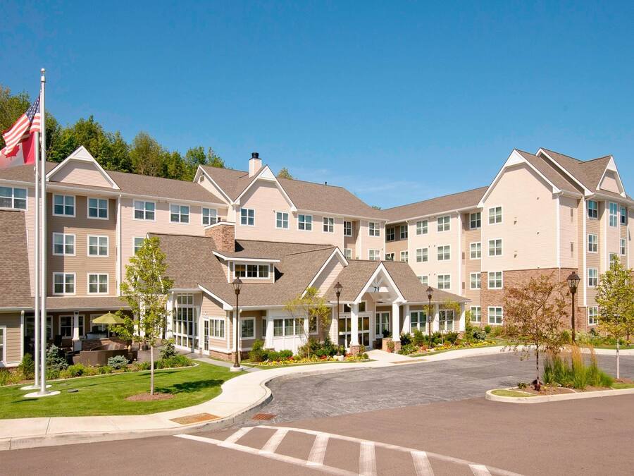 A multi-story hotel with a central courtyard, flagpoles, and a landscaped entrance area.
