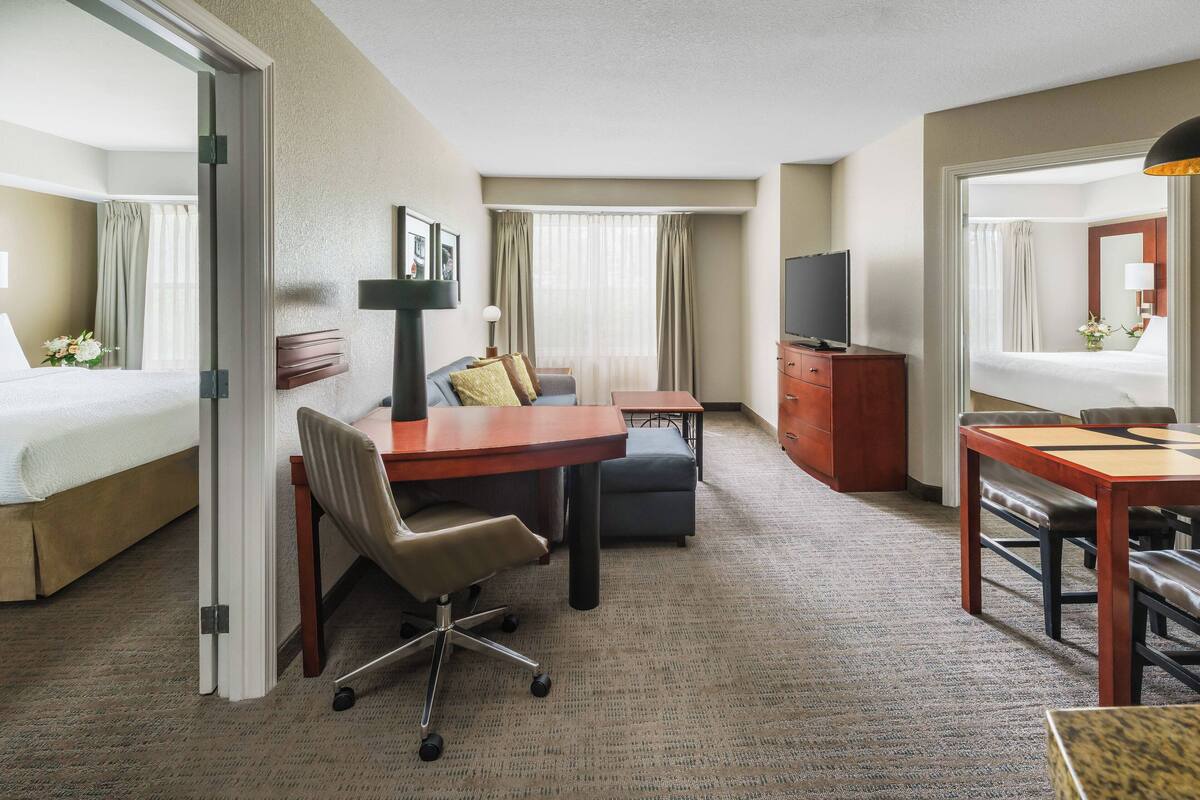 A hotel room with a bed, a desk with a chair, a television, a dresser, and a mirror.