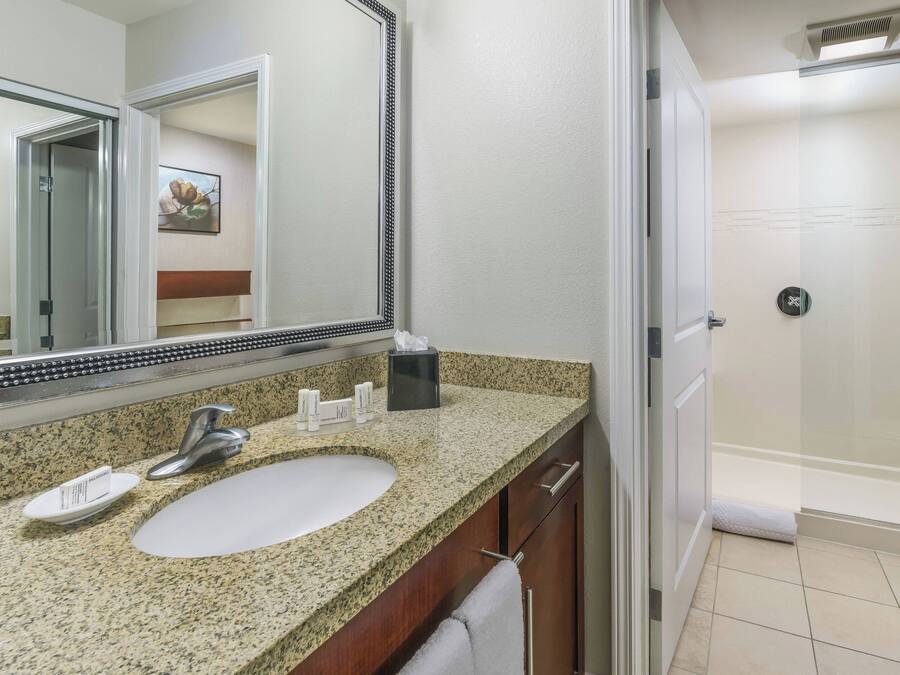 Baño con lavamanos de granito, espejo, toallero y zona de ducha.