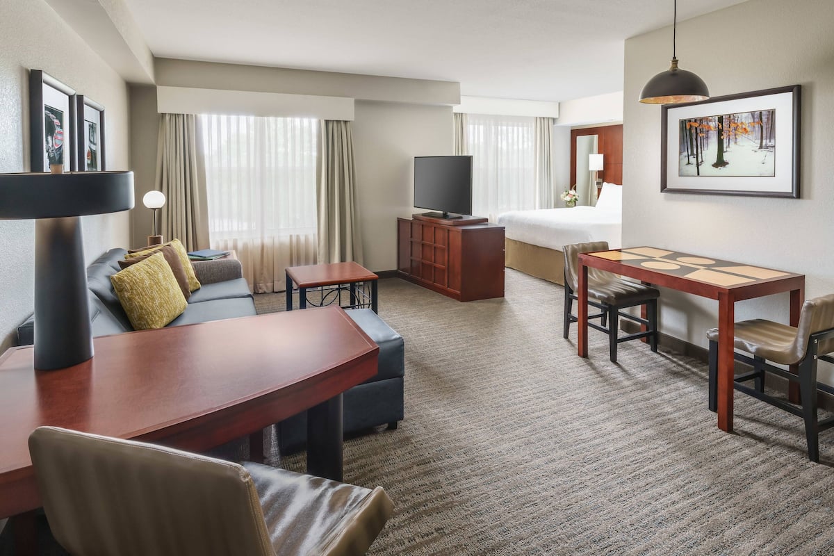 A hotel room with a sofa, a dining table, a TV, and a bed.
