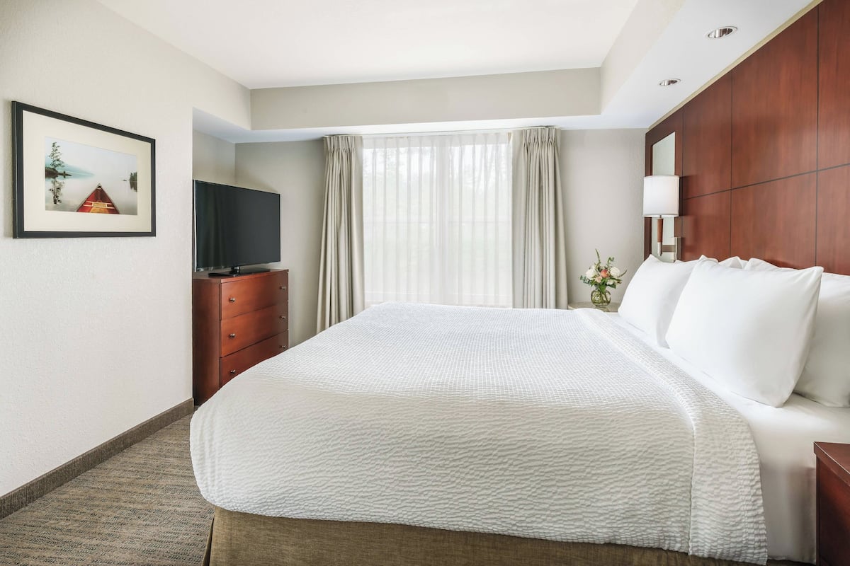 A hotel room with a large bed, a television, a wooden wardrobe, and a framed picture on the wall.