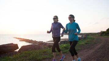 Dos personas trotando por un sendero de tierra junto a un cuerpo de agua, con rocas y vegetación de fondo.