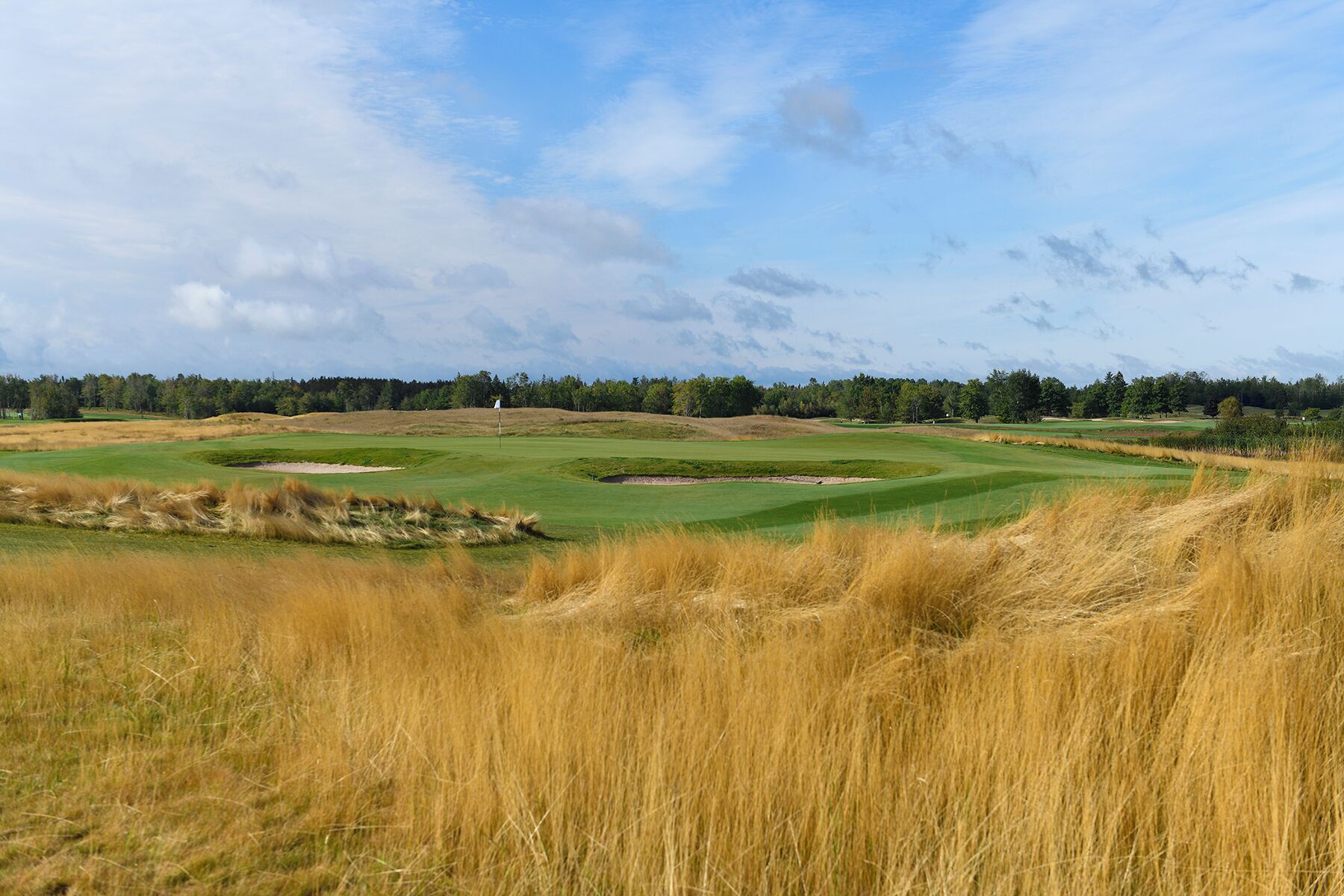 A golf course with sand bunkers, a flag, and a clear sky.