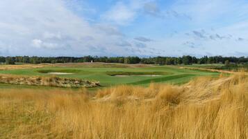 A golf course with sand bunkers, a flag, and a clear sky.