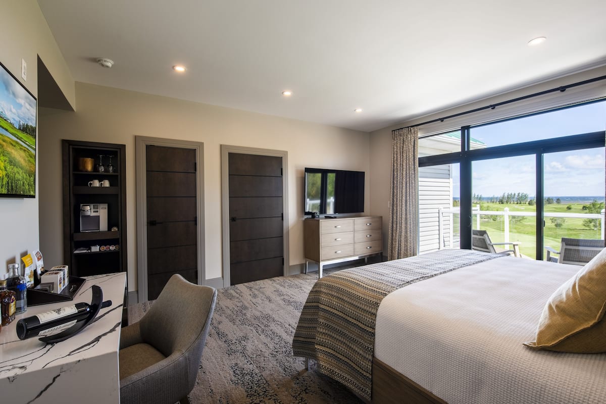 Habitación de hotel con una cama grande, un escritorio con computadora, televisión y vista a un campo de golf.