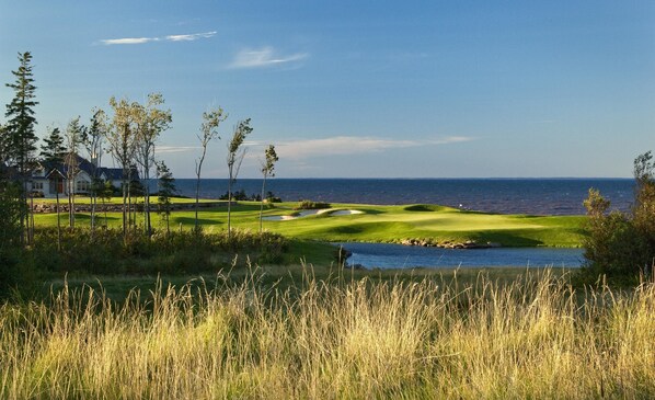 A golf course with a house in the background, a body of water, and a clear sky.