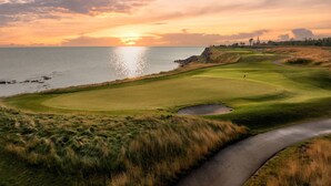 Un campo de golf con un cuerpo de agua y un atardecer.