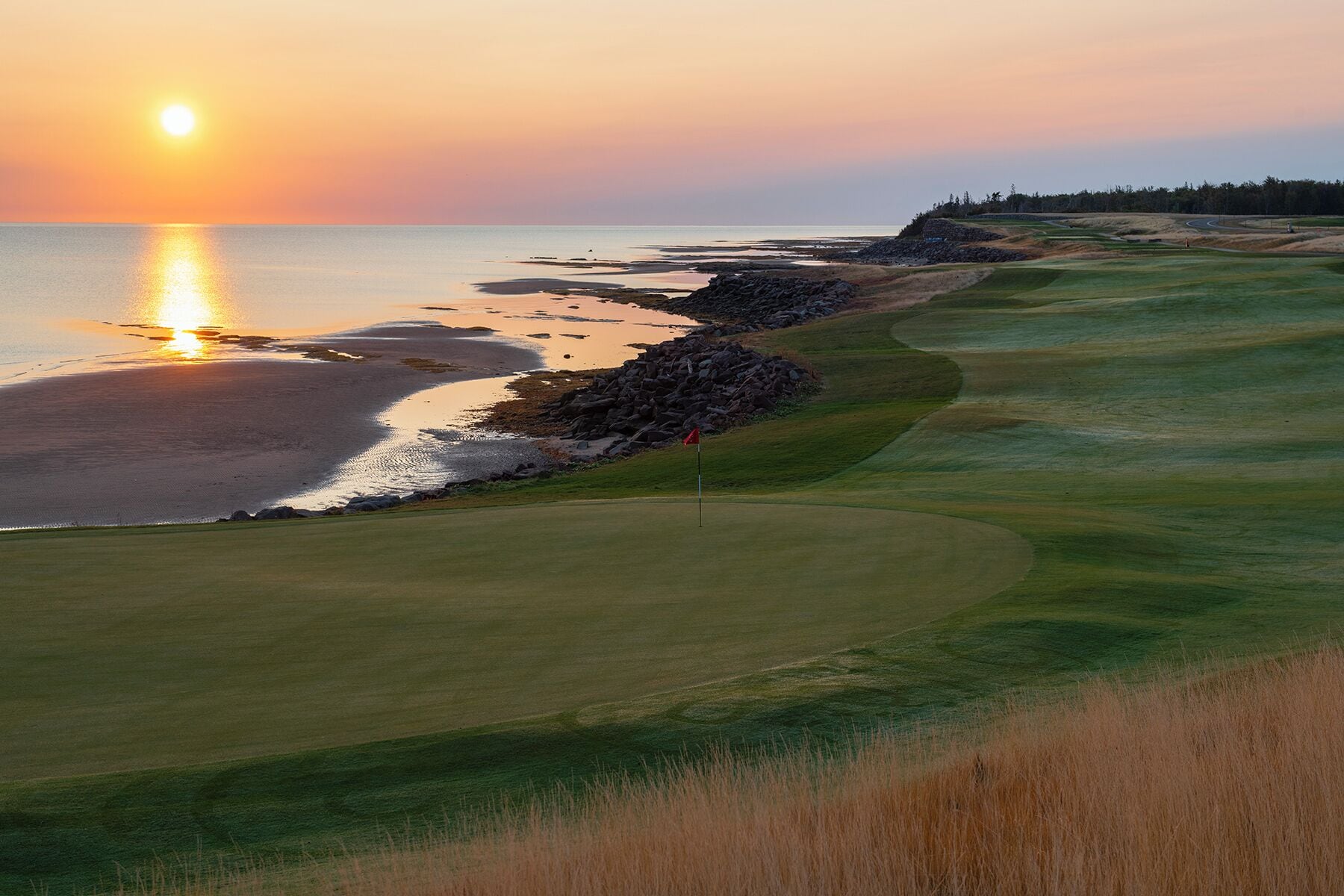 A golf course with a view of the ocean at sunset.