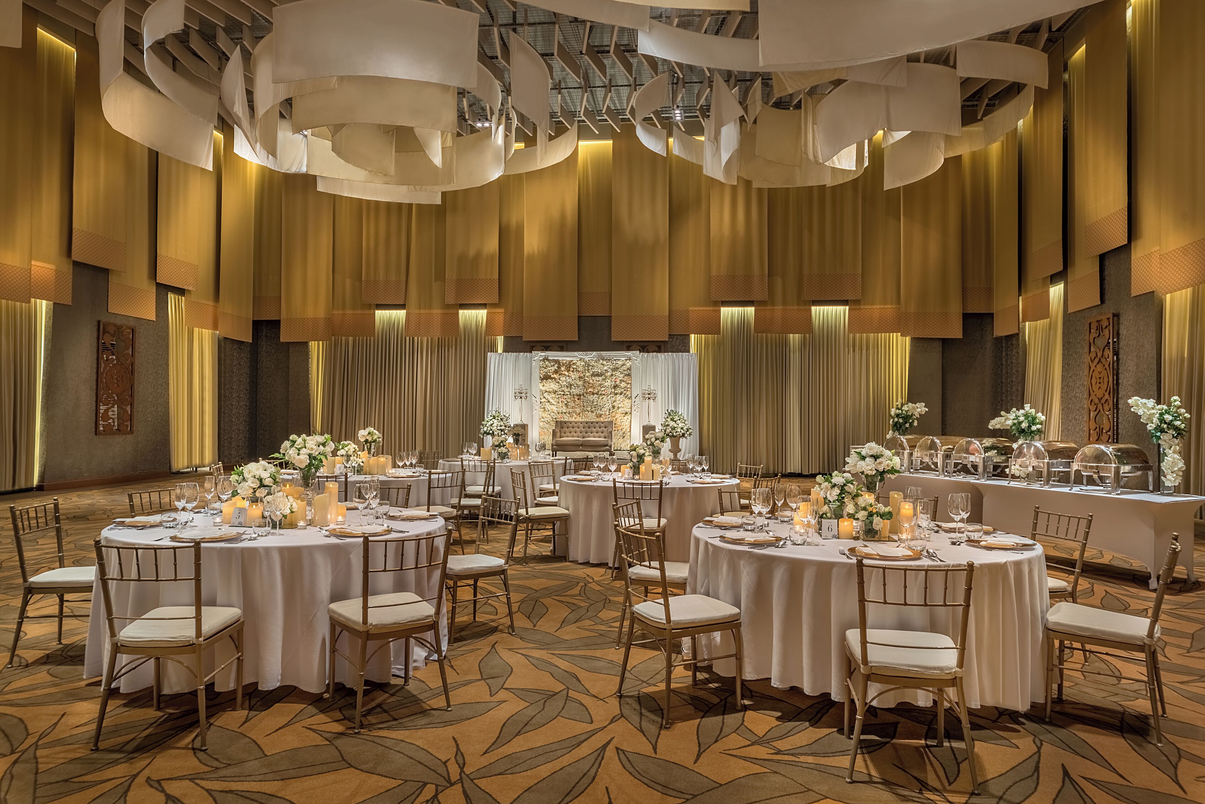 A banquet hall with round tables set for dining, featuring white tablecloths and floral centerpieces.
