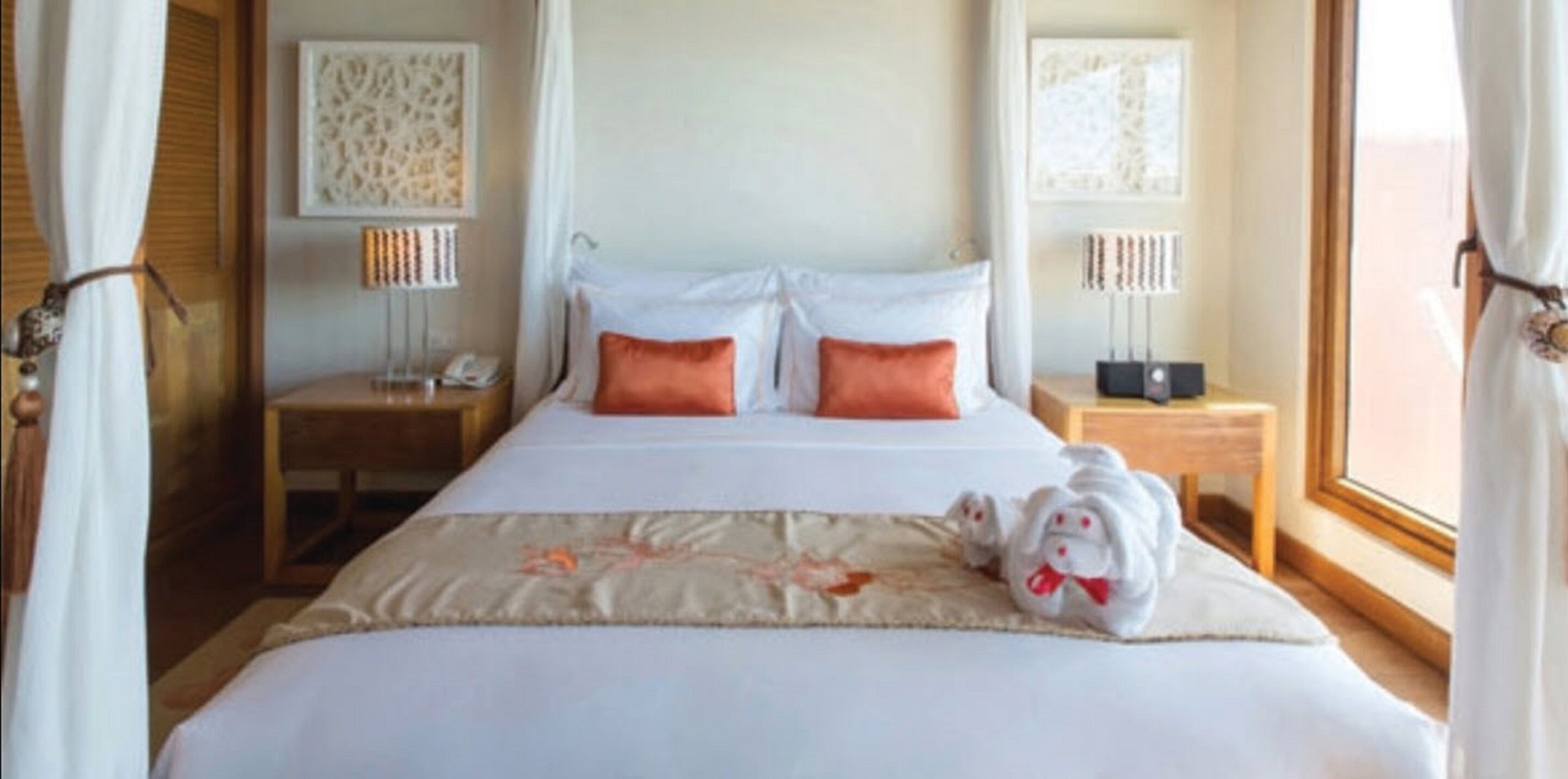 A hotel room with a bed, two bedside tables, a nightstand, a lamp, and a window with curtains.