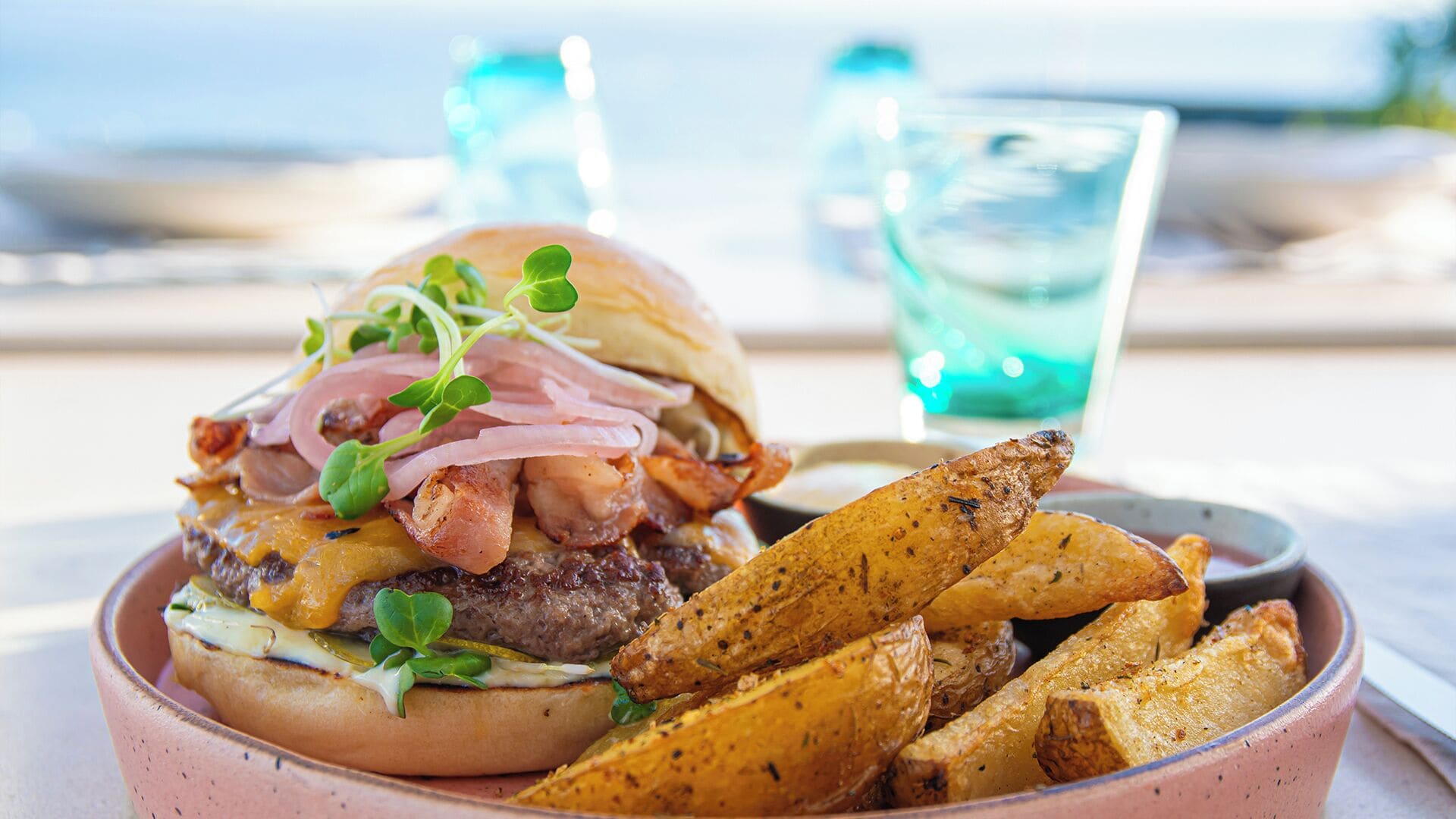 A burger with bacon, cheese, and greens, served with roasted potatoes.